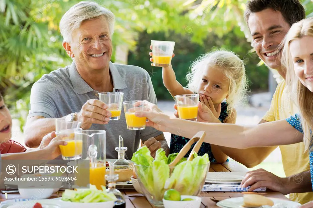 Multi_generation family toasting with orange juice outdoors, portrait