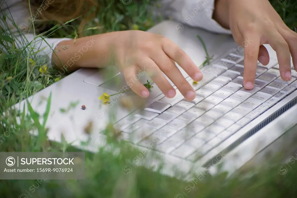 Girl using laptop computer in grass, cropped