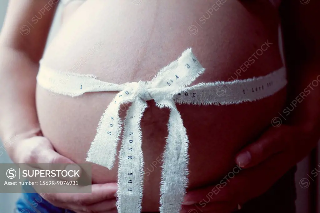 Pregnant woman with ribbon wrapping around stomach, mid section