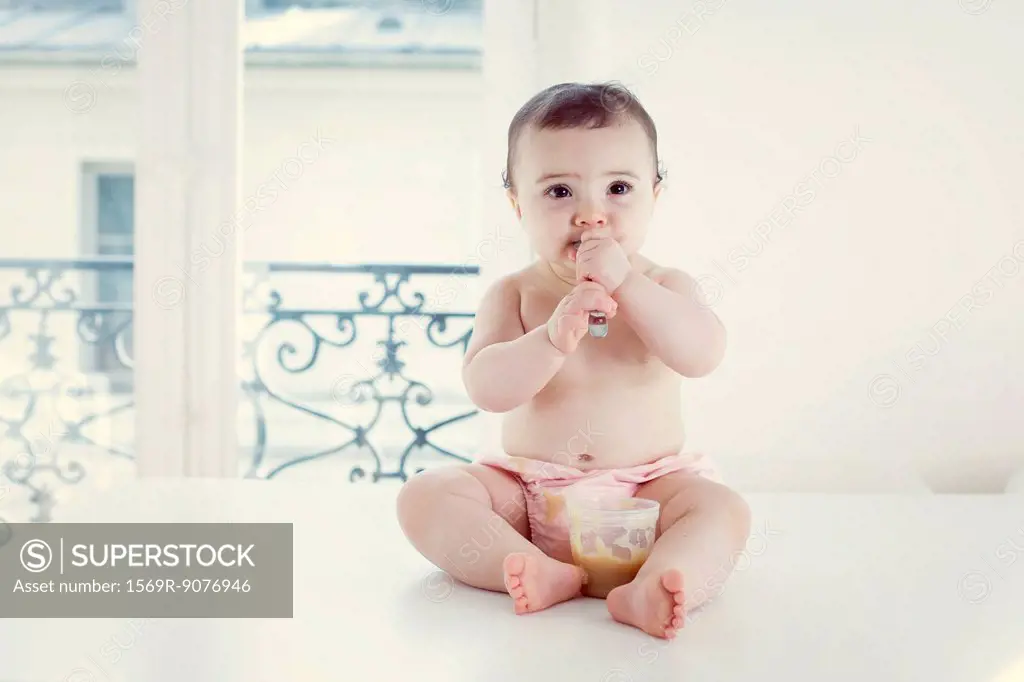 Infant eating baby food with spoon, portrait