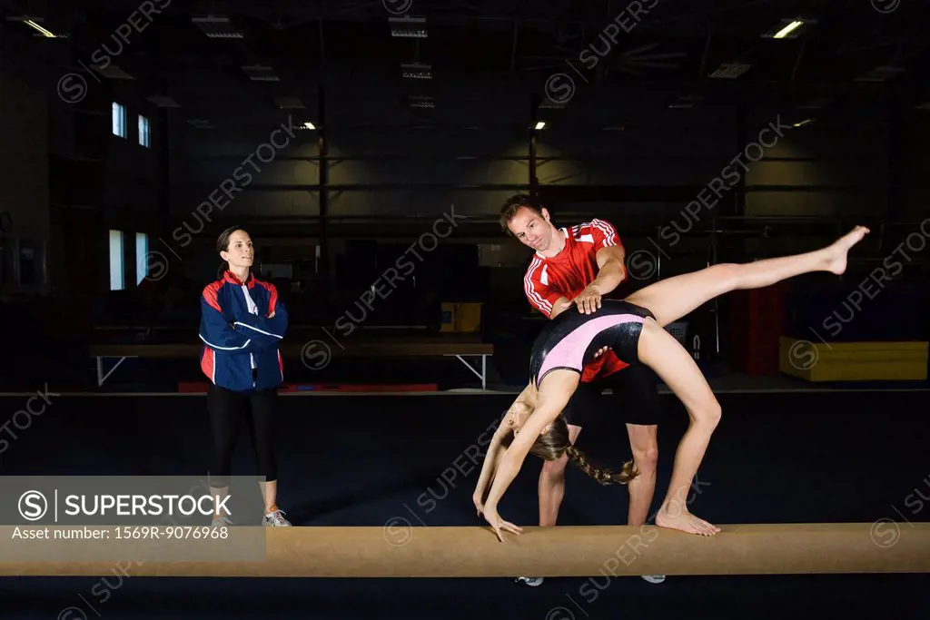 Female gymnast practicing on balance beam with coach