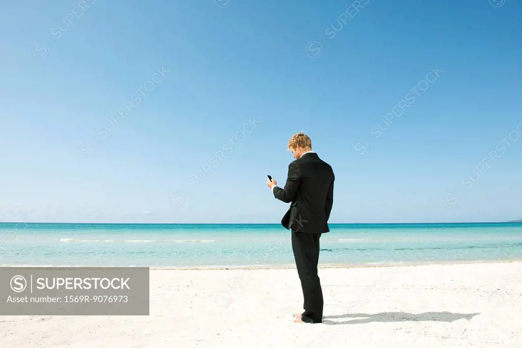 Businessman using cell phone on beach