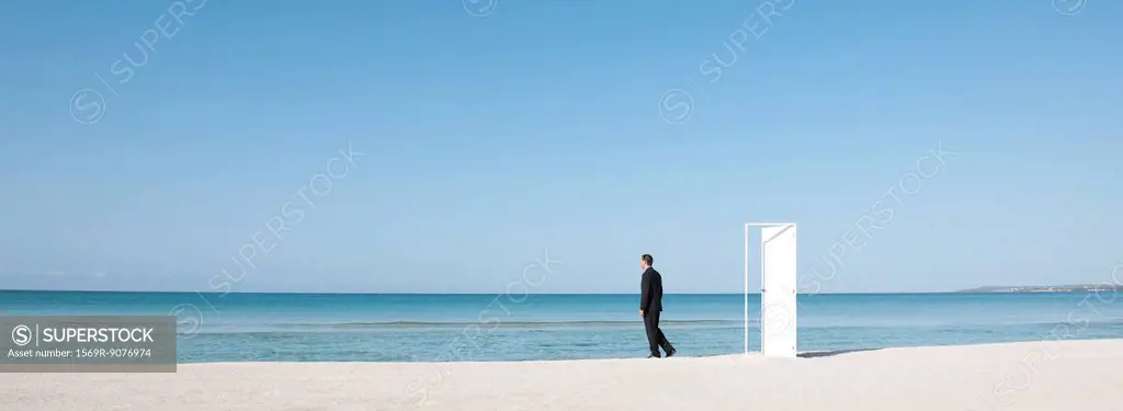 Businessman standing on beach next to half_open door, looking at ocean