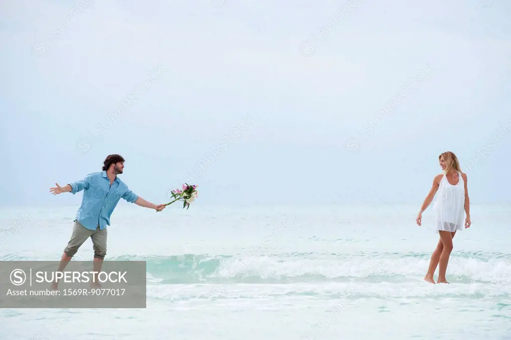 Couple walking apart in sea, man holding out bouquet