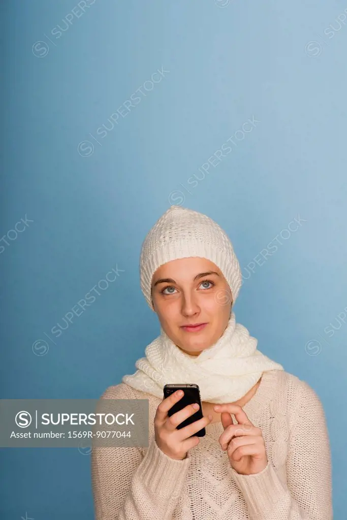 Young woman using cell phone, looking up in thought