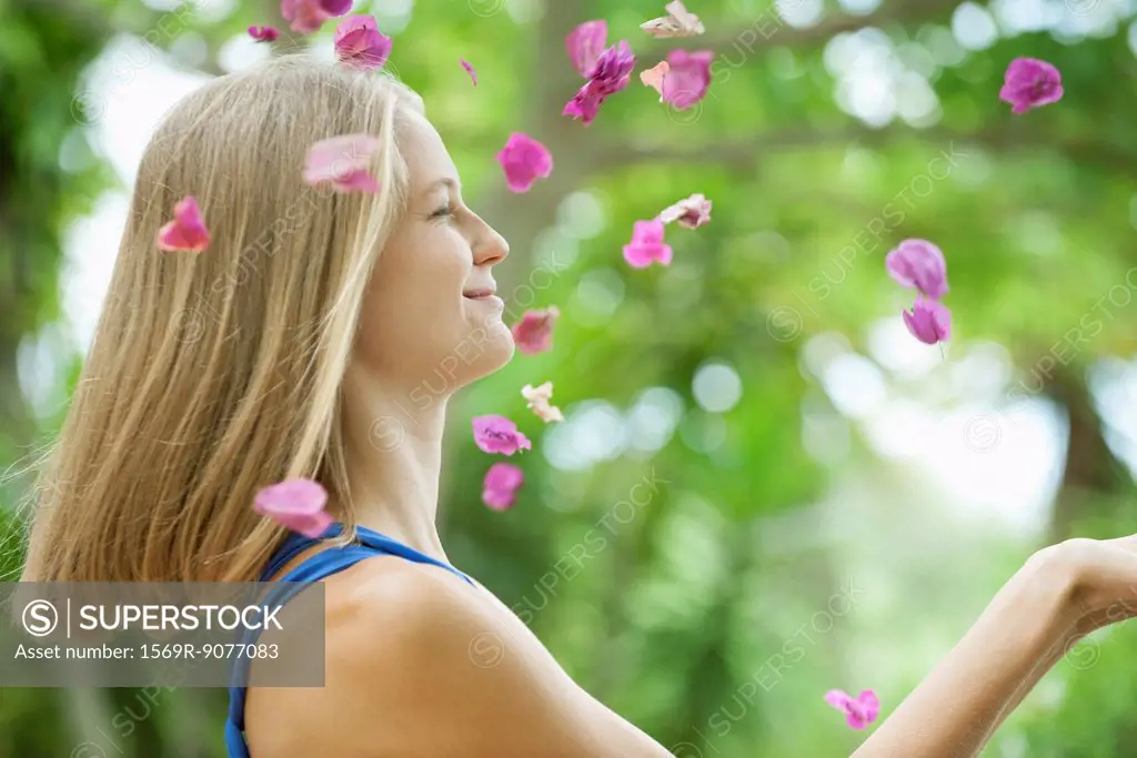 Young woman throwing petals in air, side view