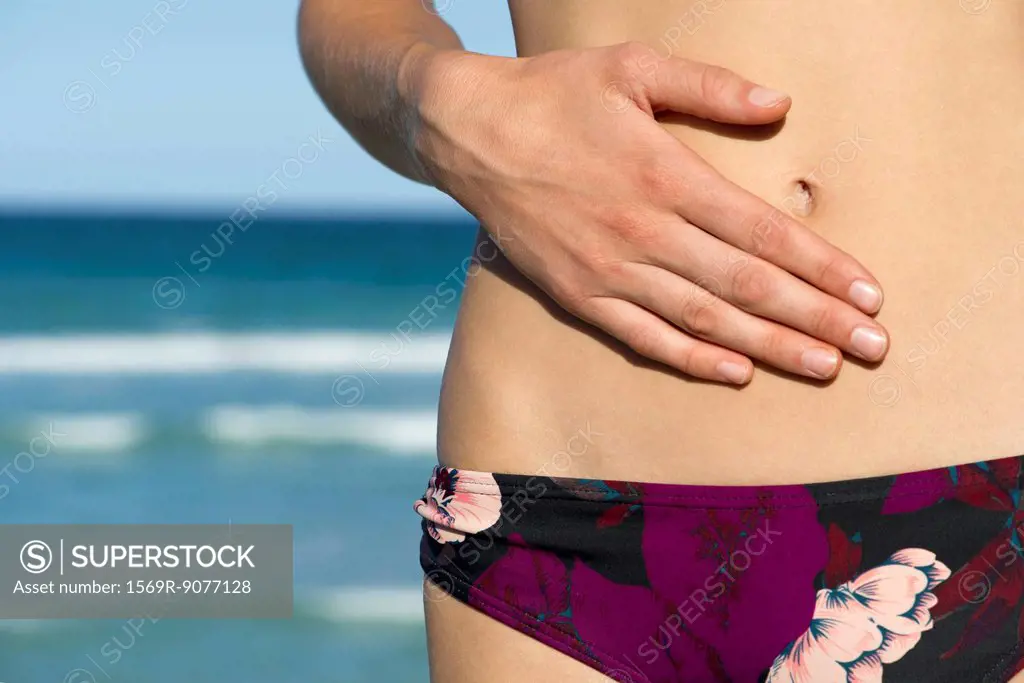 Woman in bikini bottom, hand on abdomen, mid section