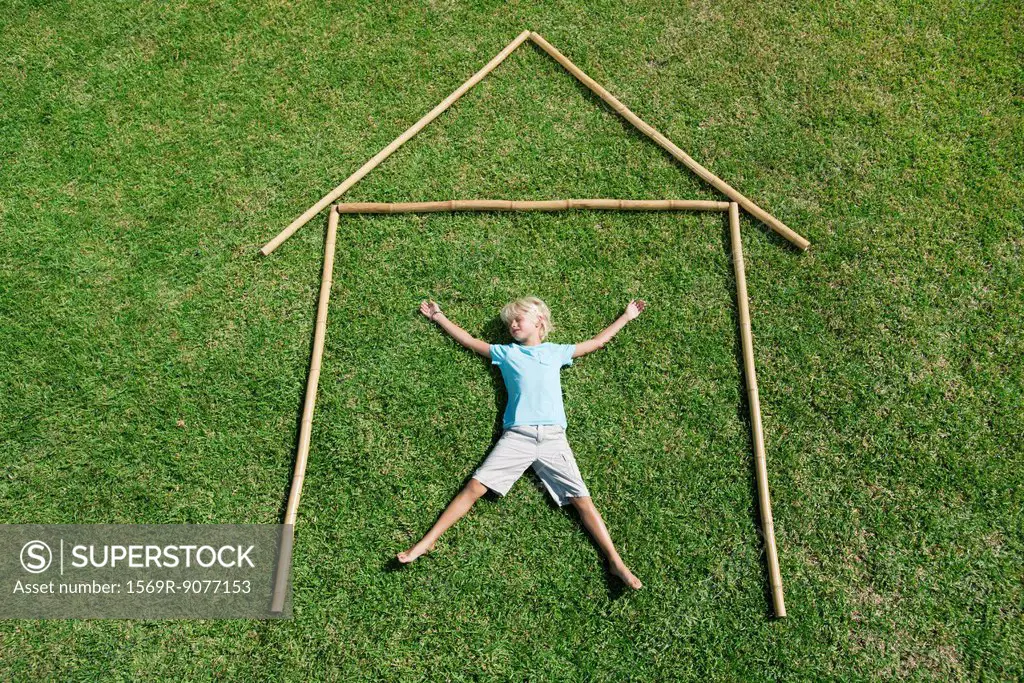 Boy lying on grass within outline of house, high angle view