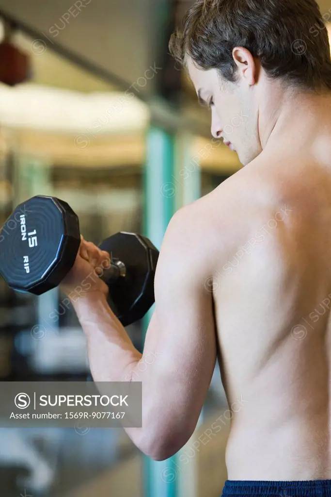 Barechested young man lifting dumbbell, rear view
