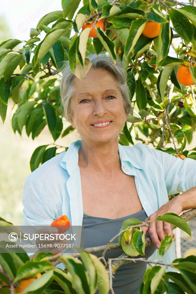 Senior woman smiling under persimmon tree, portrait