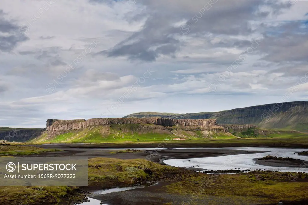 Iceland, stream running through lava field, basalt cliffs in the distance