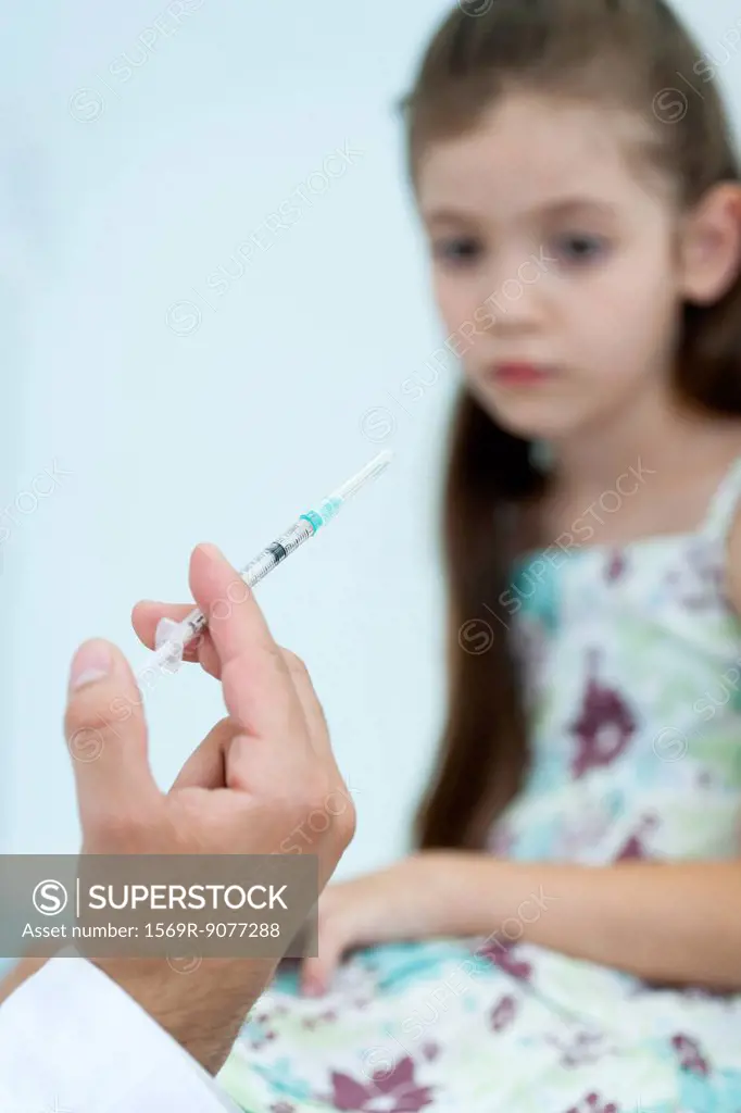 Doctor´s hand holding syringe, girl sitting in background
