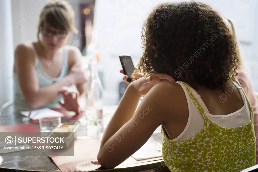 Young woman text messaging in cafe, rear view
