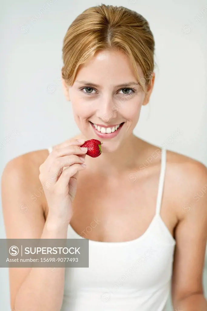 Young woman eating strawberry, portrait