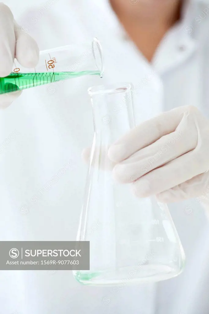 Scientist pouring liquid from graduated cylinder to conical flask