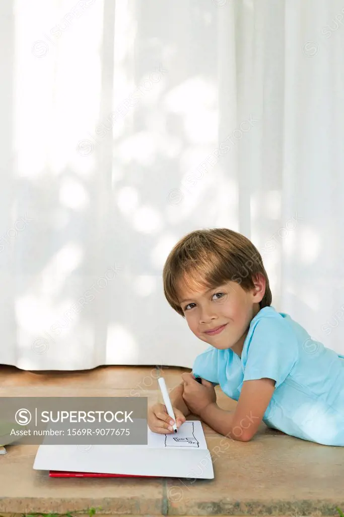 Boy lying on ground, drawing in notebook