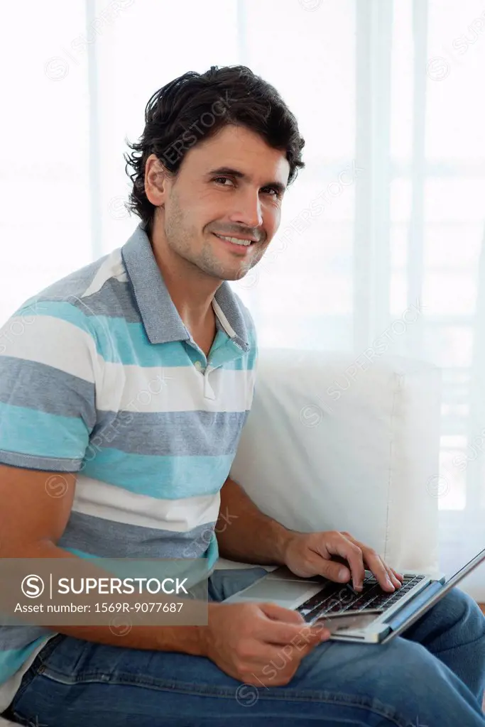 Man holding credit card while using laptop computer, portrait