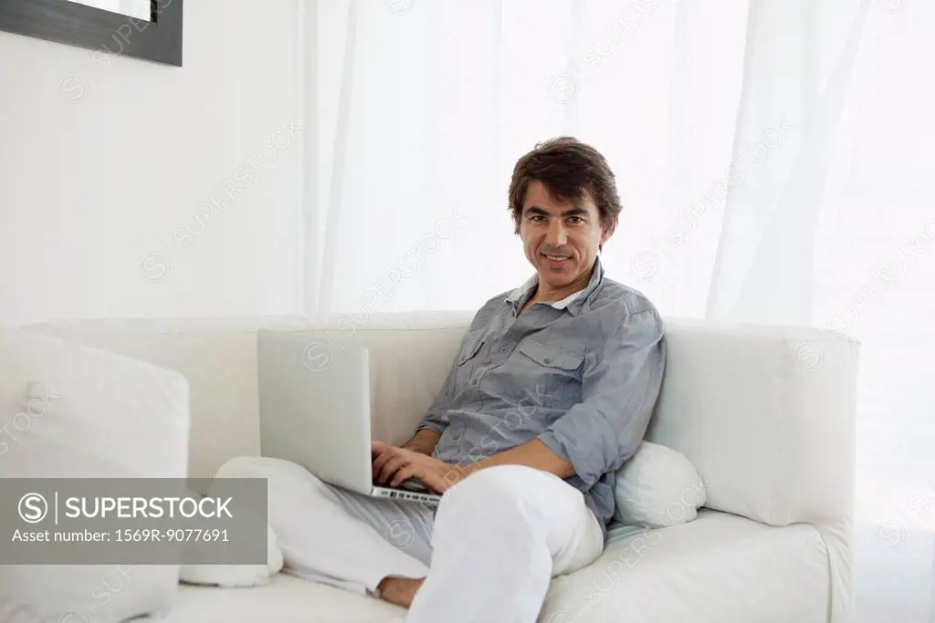 Mature man using laptop computer on sofa, portrait