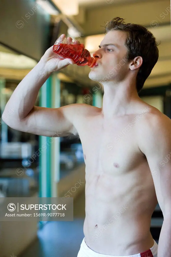 Barechested young man drinking sports drink