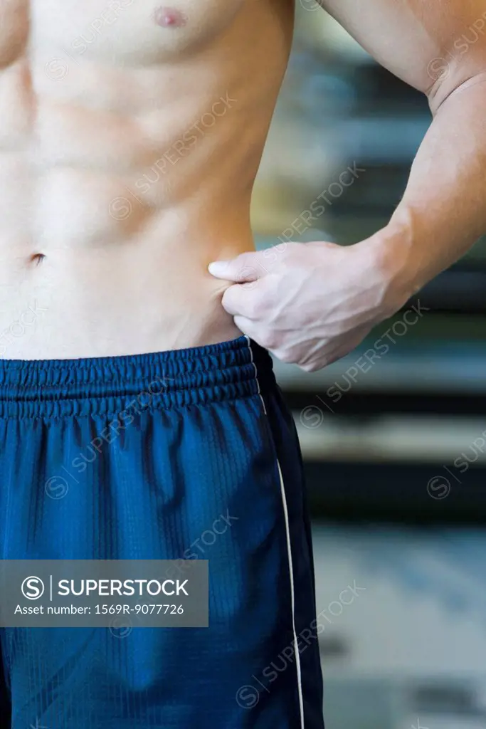 Barechested man pinching waist, mid section