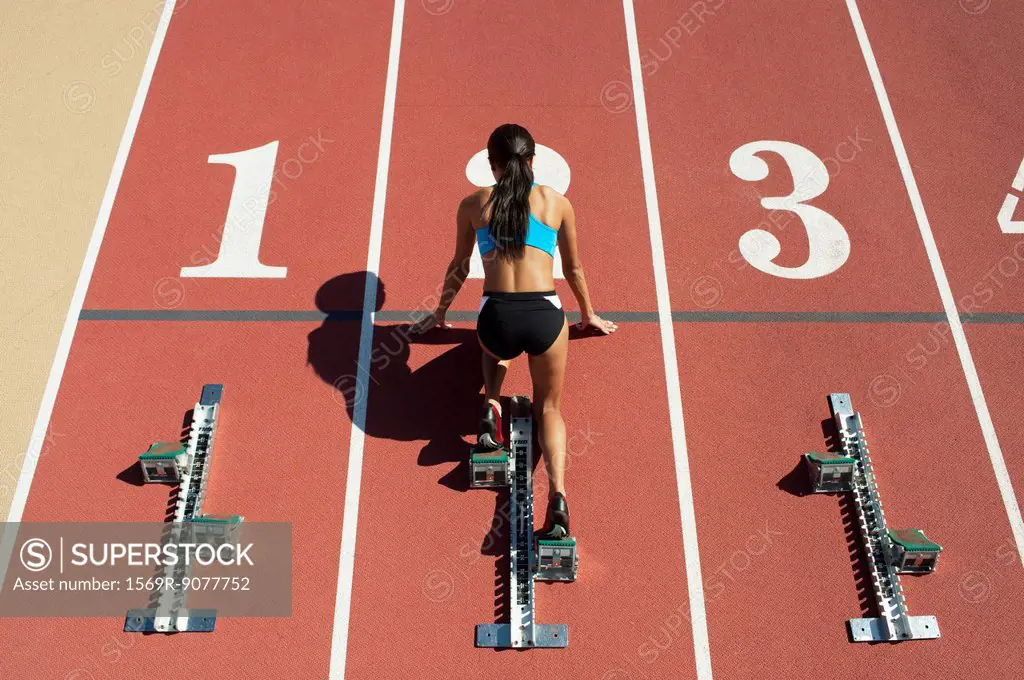 Female athlete in starting position on running track, rear view