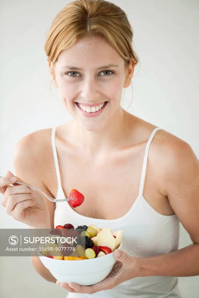 Young woman eating bowl of fruit, portrait