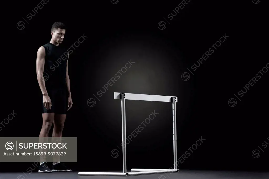 Male athlete standing behind hurdle