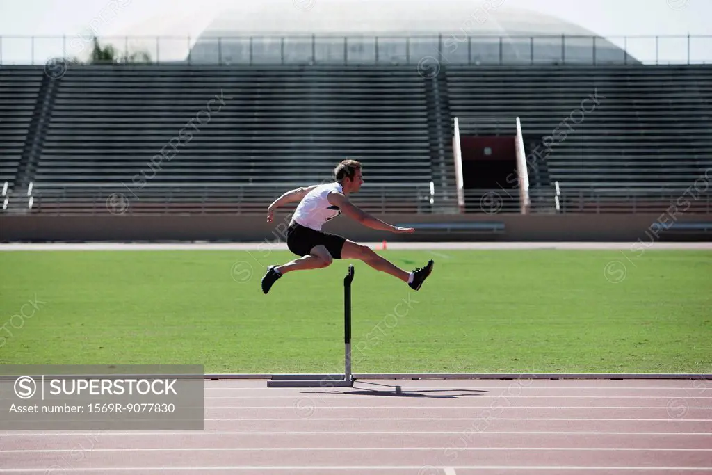 Male athlete clearing hurdle, side view