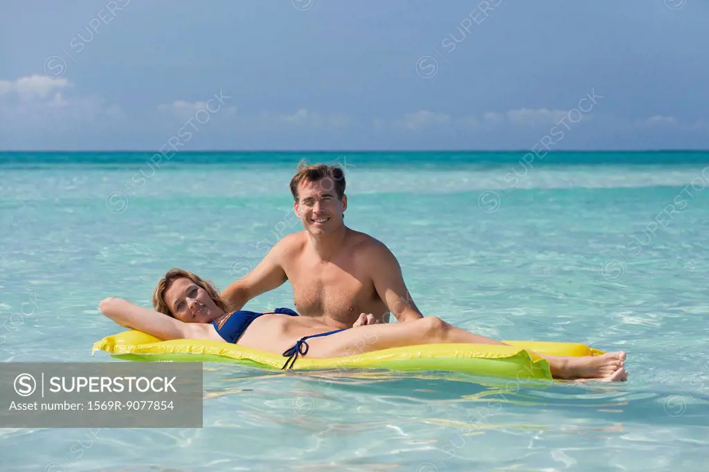 Couple relaxing in ocean, woman lying on pool raft, portrait