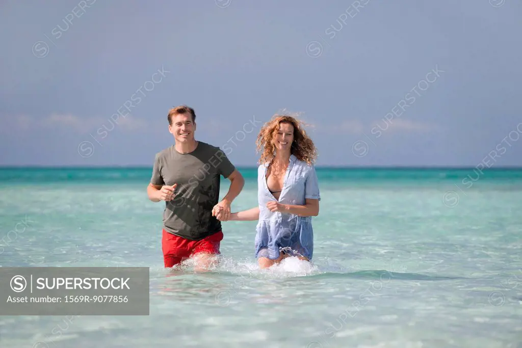 Couple standing knee deep in water, holding hands