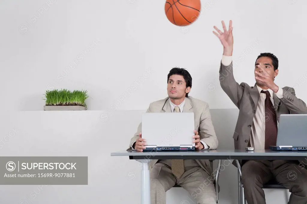 Young businessman watching colleague throwing basketball