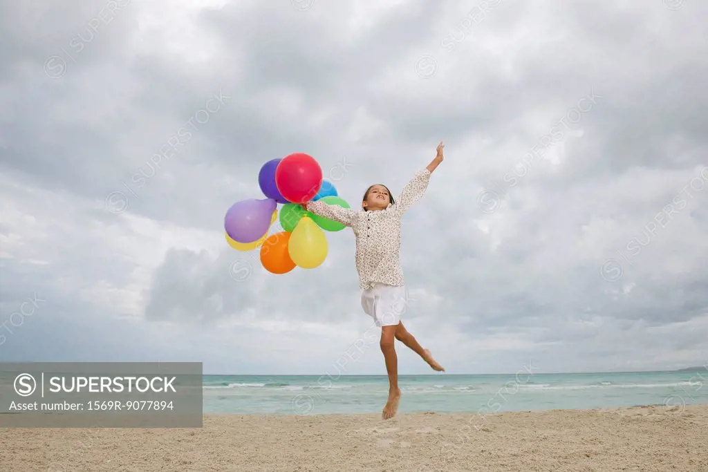 Girl jumping on beach with bunch of colorful balloons