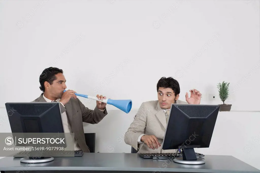 Businessman blowing vuvuzela horn into colleague´s ear