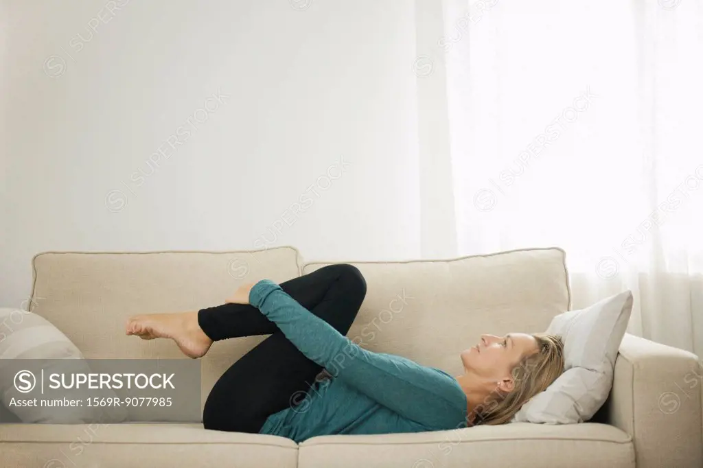 Mature woman lying on couch hugging knees