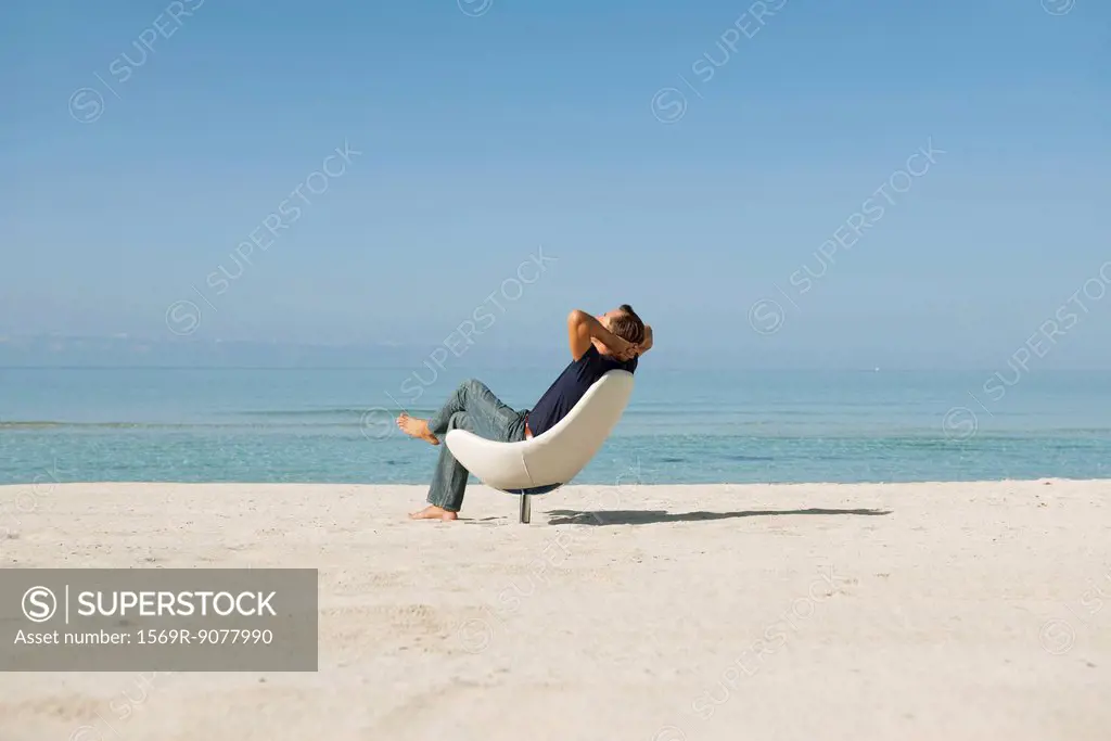 Mid_adult man relaxing in armchair on beach