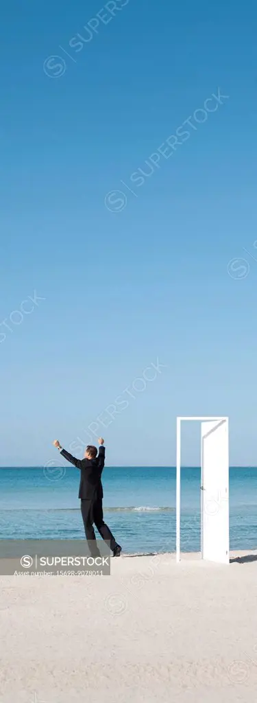 Businessman standing on beach looking at ocean with arms raised