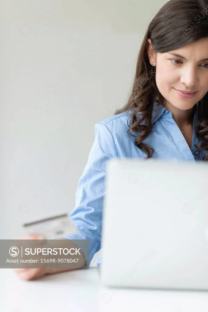 Mid_adult woman holding credit card while using laptop computer