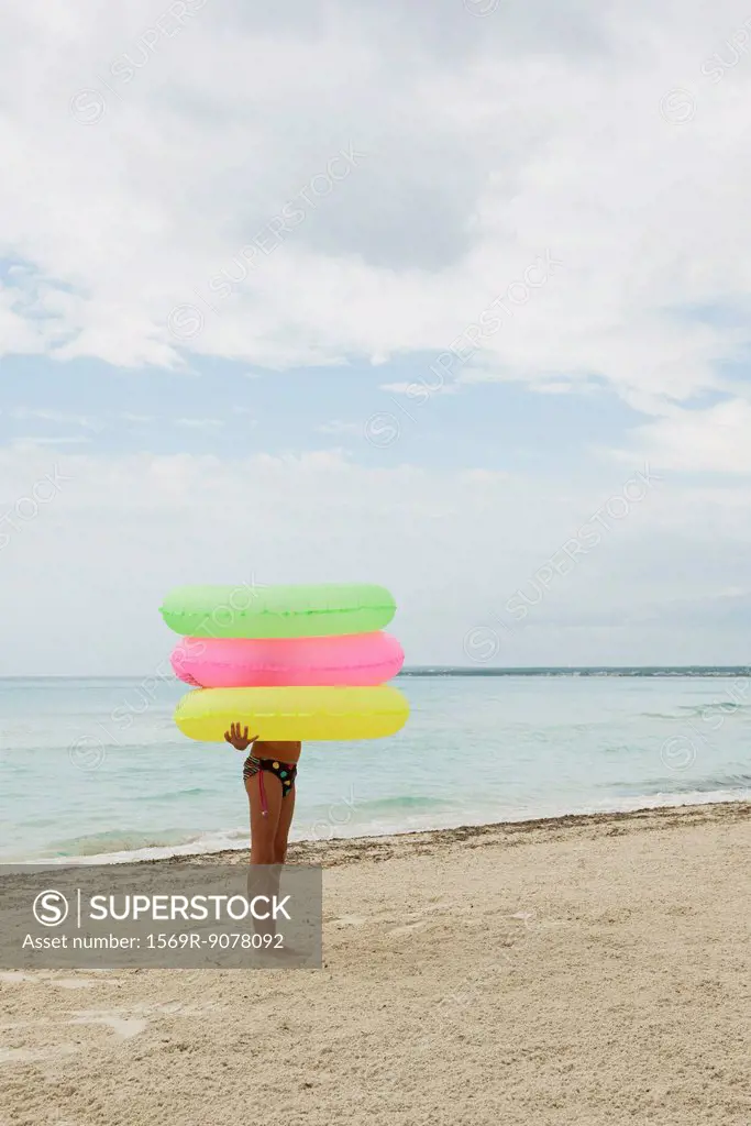 Girl holding stack of inflatable rings on beach, face obscured