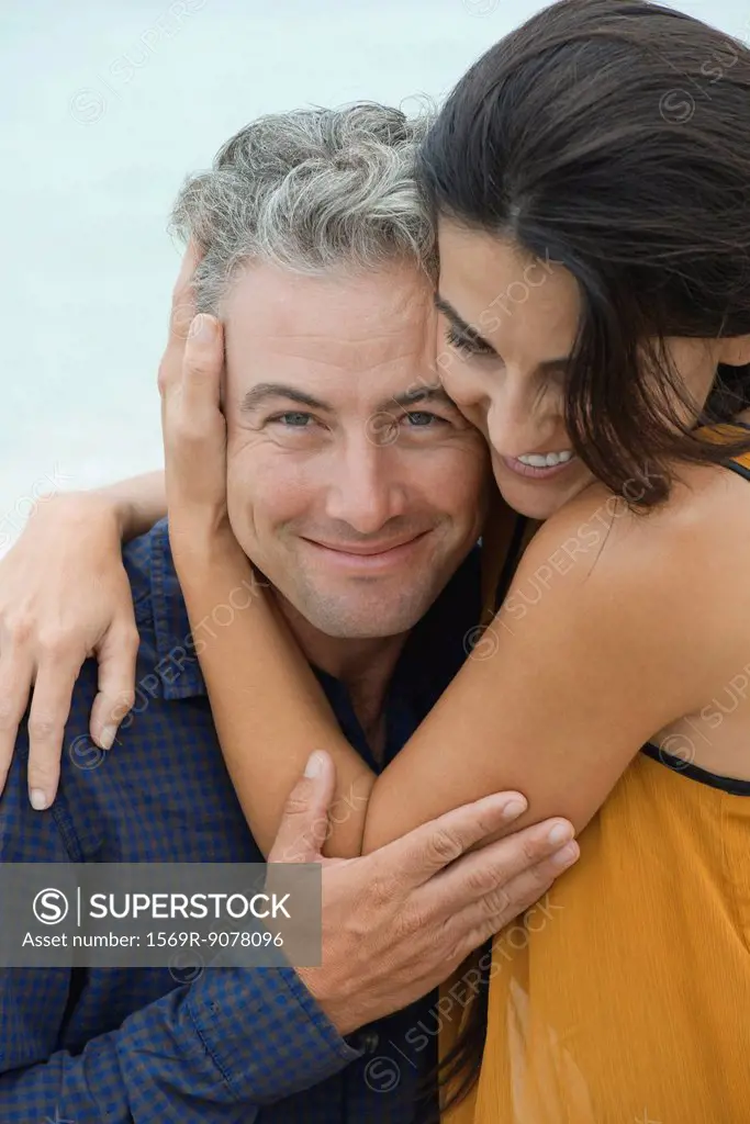 Woman wrapping arms around husband, portrait