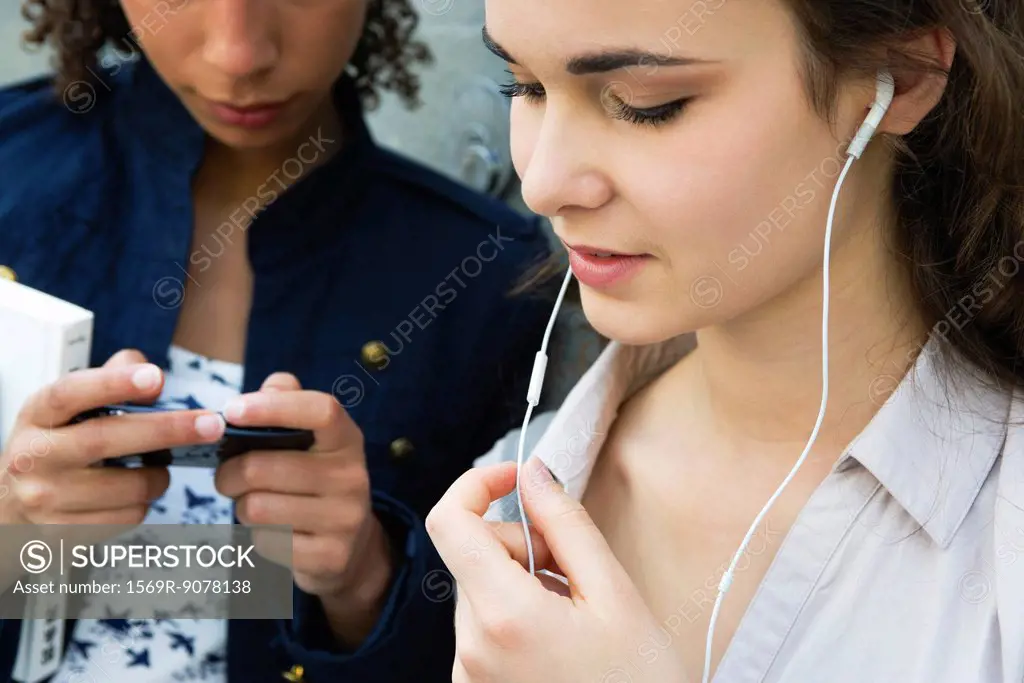 Young woman standing with friend, listening to earphones
