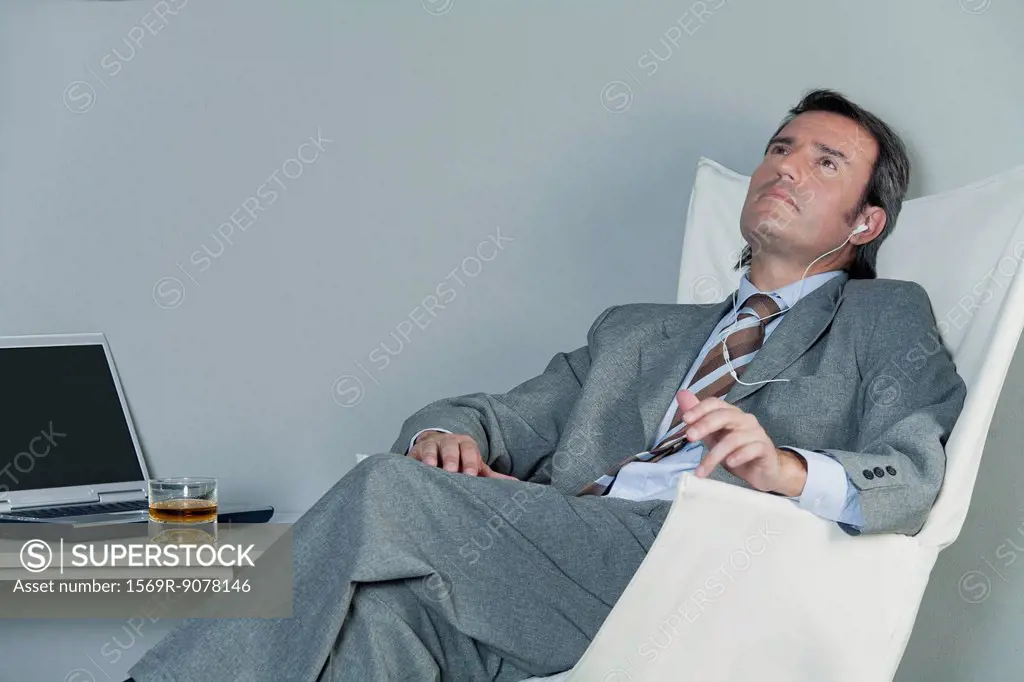 Mature businessman relaxing on chair with earphones