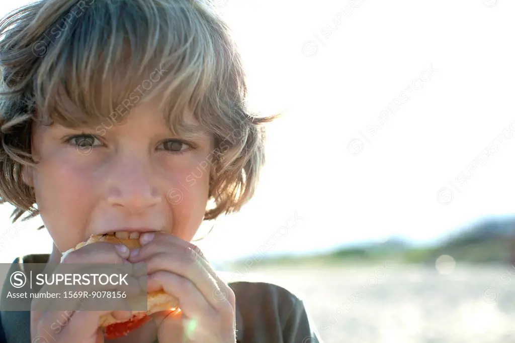 Boy eating sandwich outdoors, portrait