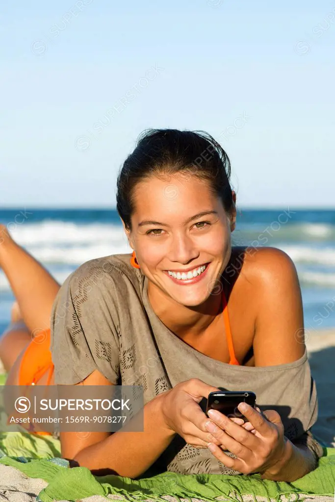 Young woman using cell phone on beach, portrait