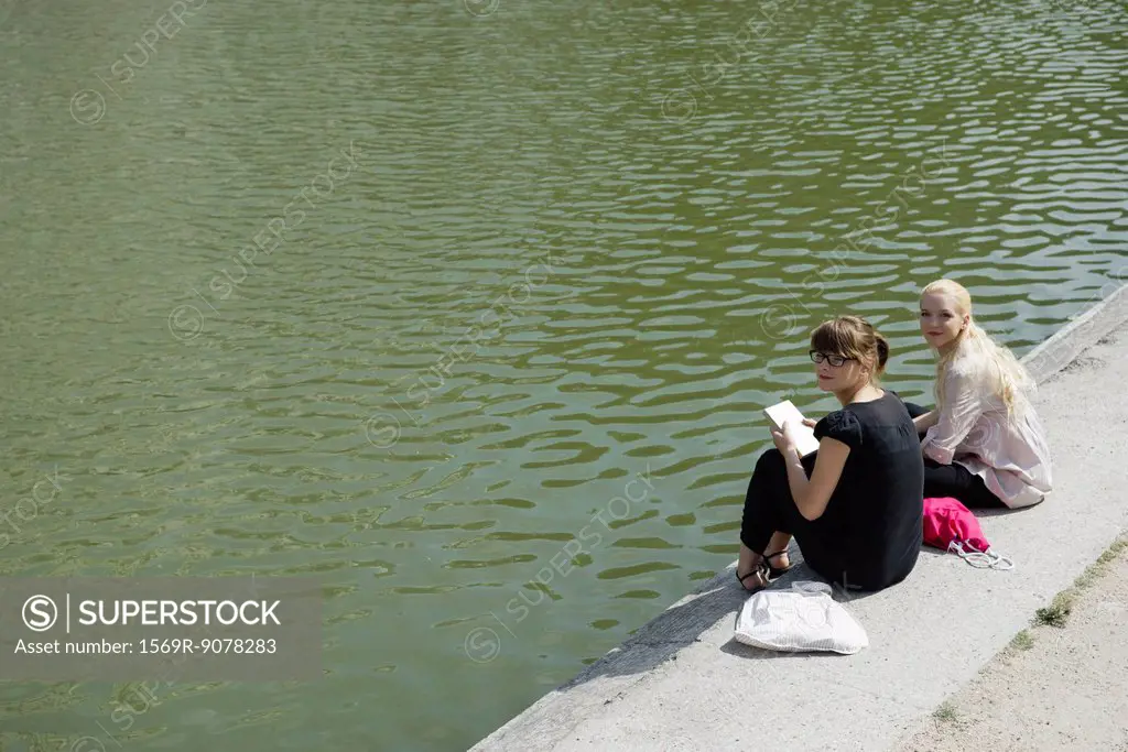 Young women sitting beside lake together