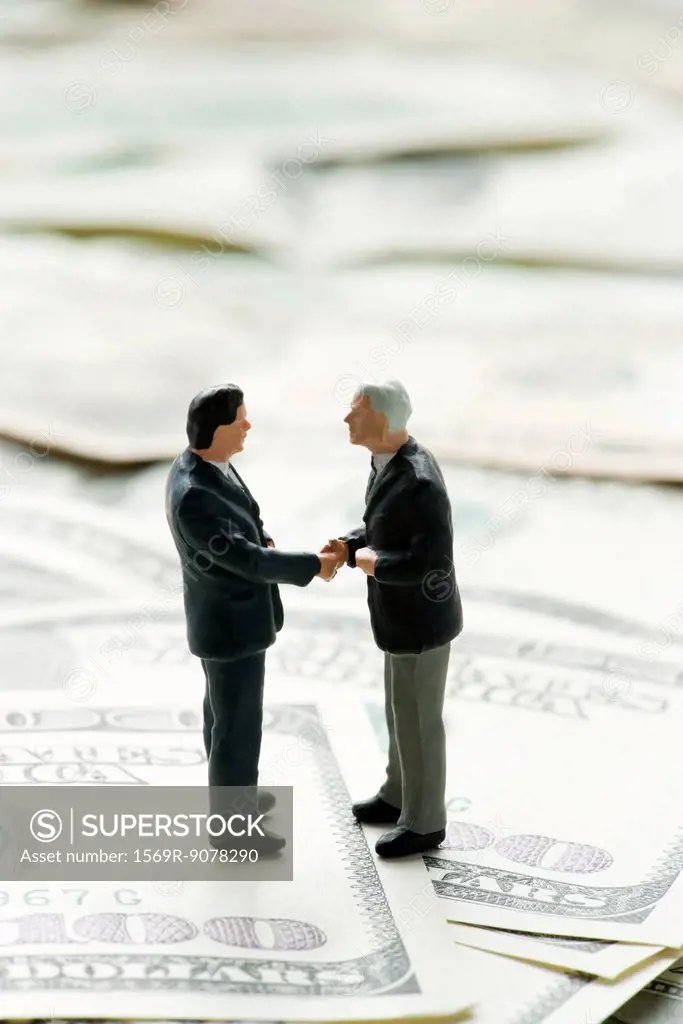 Male figurines shaking hands on pile of one hundred dollar bills