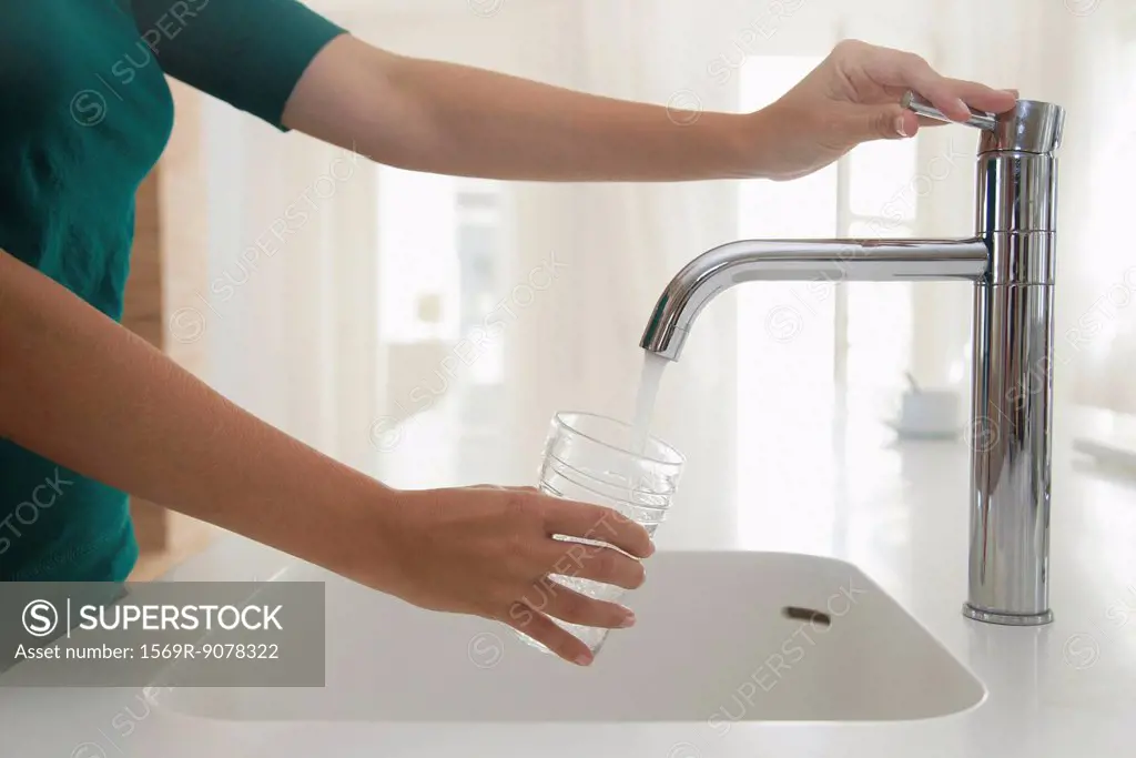 Woman filling glass of water at kitchen sink, cropped