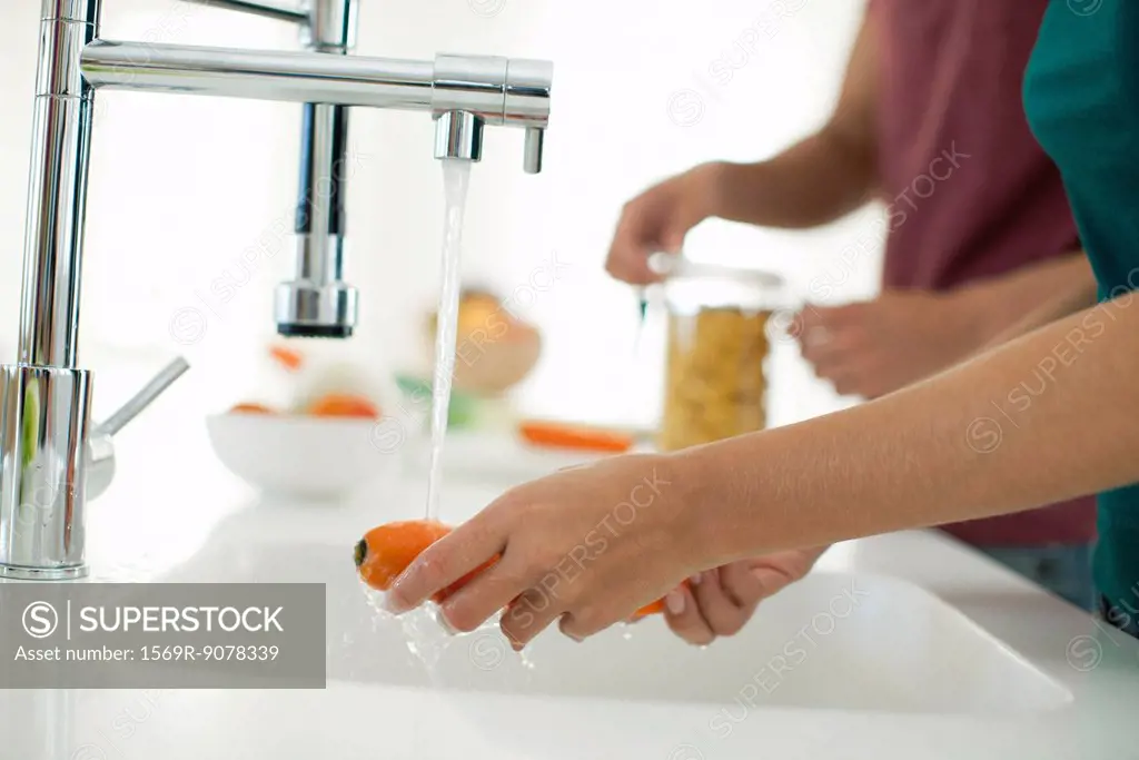 Woman washing carrot, cropped