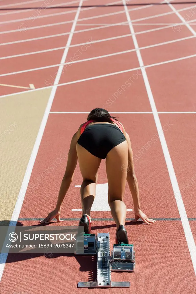 Woman crouched in starting position on running track, rear view