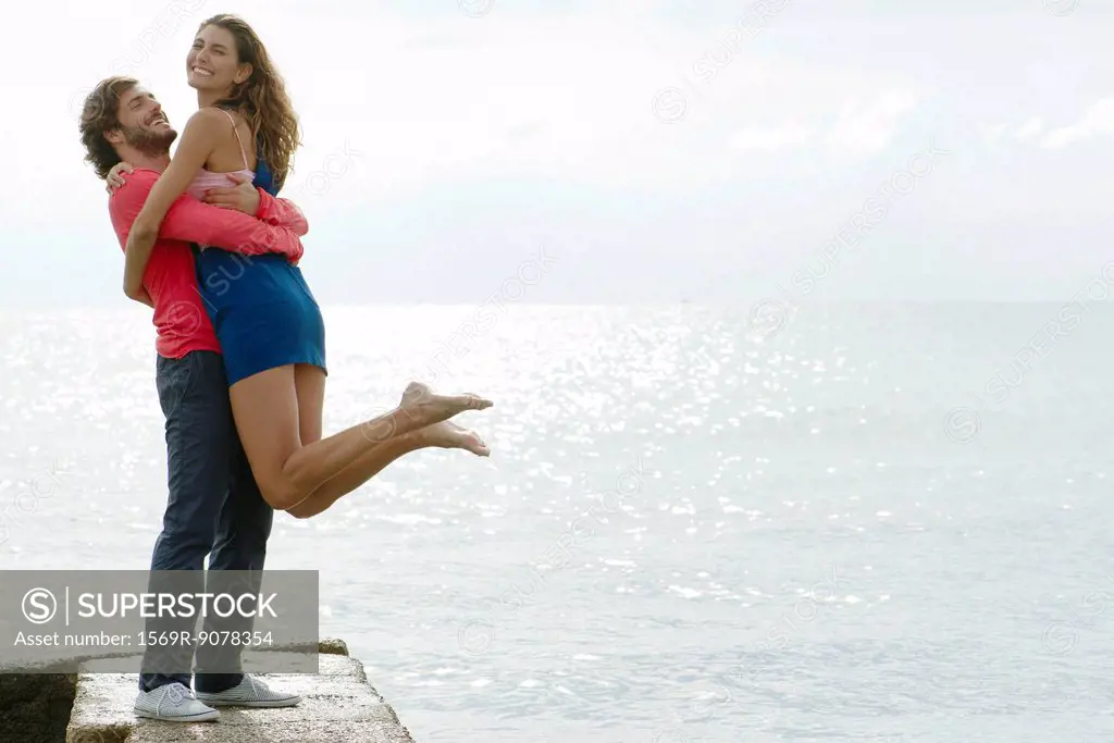 Young man lifting girlfriend up by water, portrait