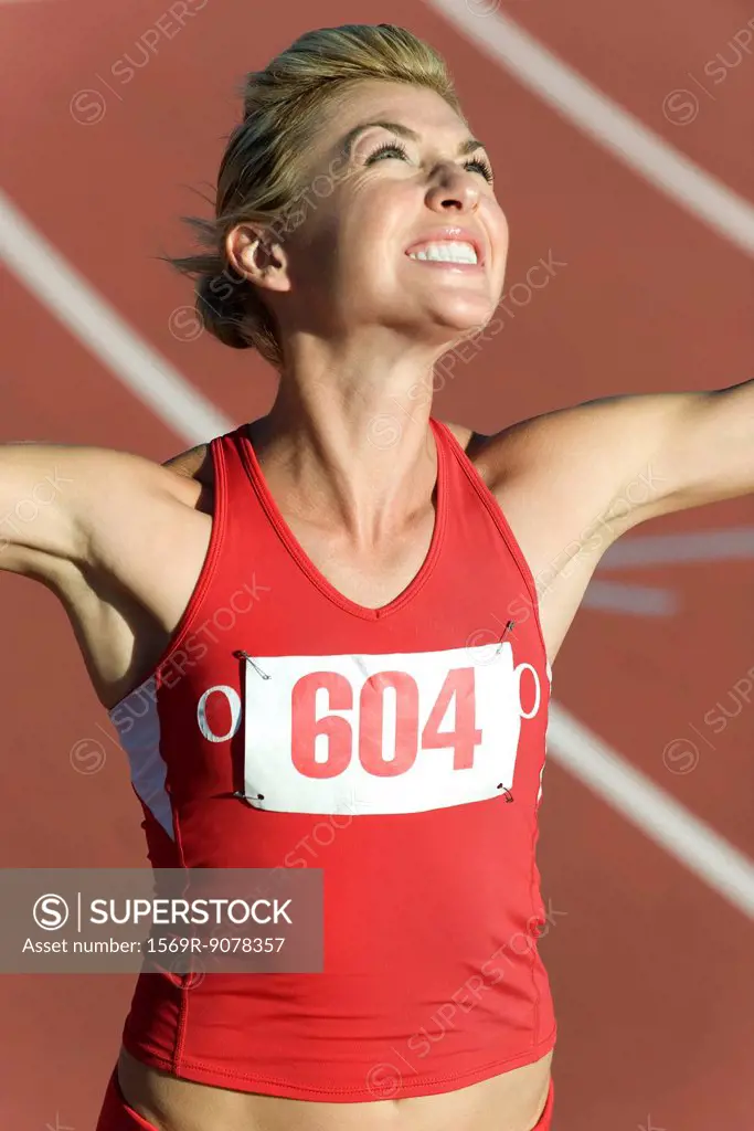 Woman running on track, looking up victoriously